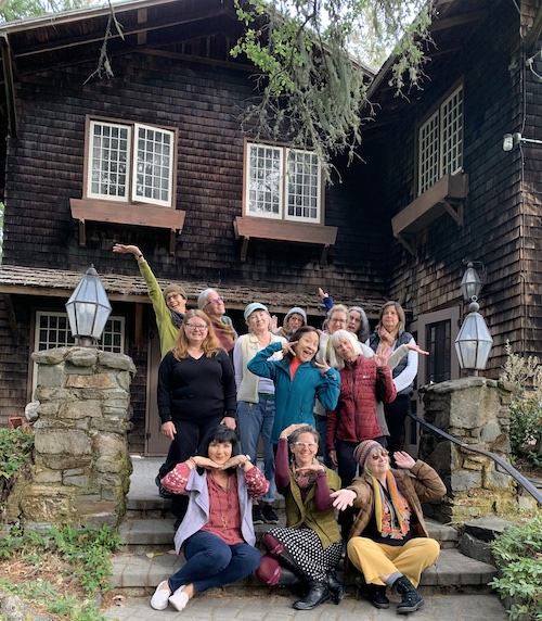 People standing and sitting on stairs in front of a shingled building in the redwoods, striking silly poses