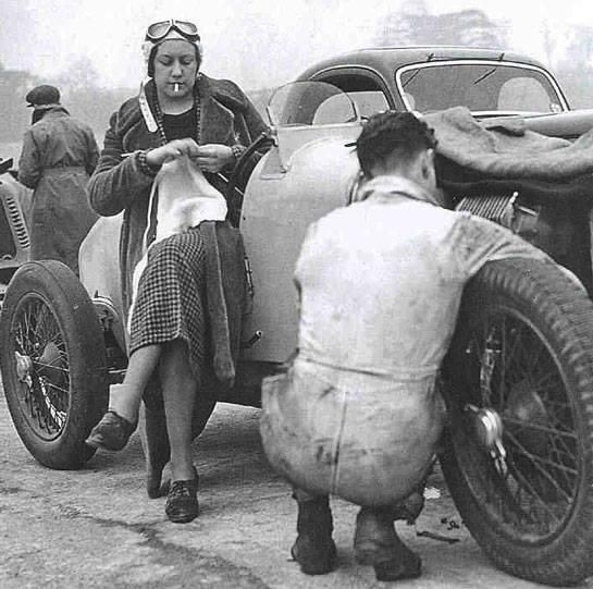 Racecar driver knitting while the tire on her racecar is changed